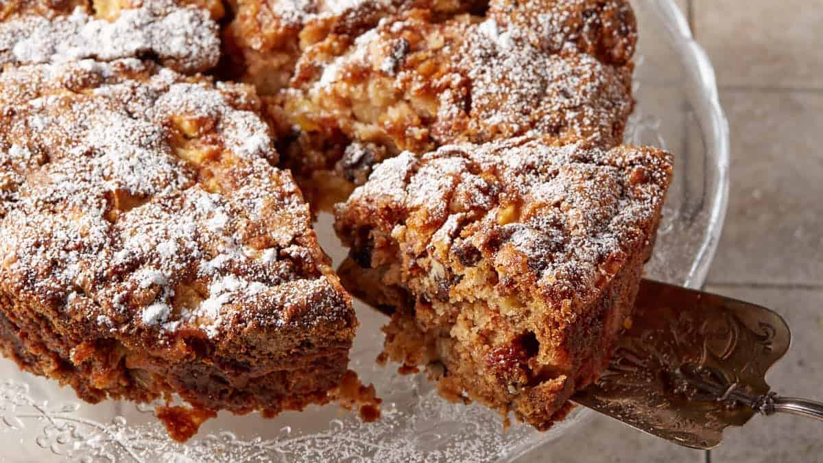 Cinnamon apple cake on a platter with a slice being removed.