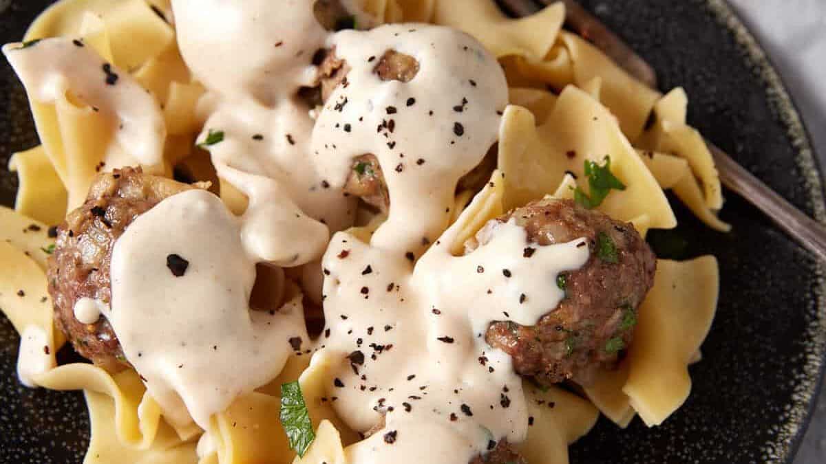 A serving platter with egg noodles and meatballs with gravy.