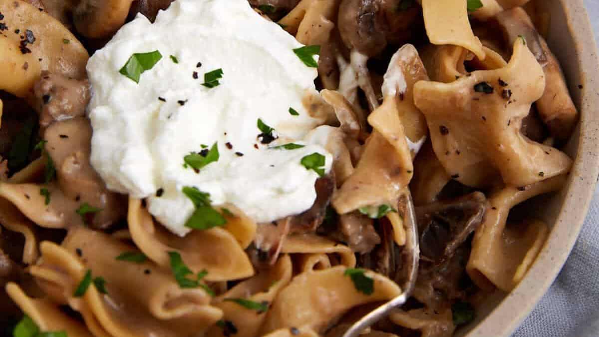 A bowl of beef stroganoff topped with sour cream.