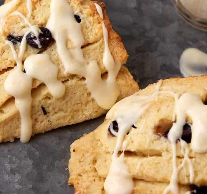 Two blueberry scones with creme fraiche next to a container of frosting.