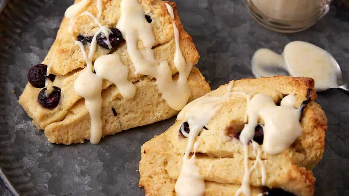 Two blueberry scones with creme fraiche next to a container of frosting.