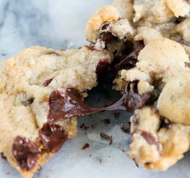 A single chocolate chip cookie with a piece broken off.