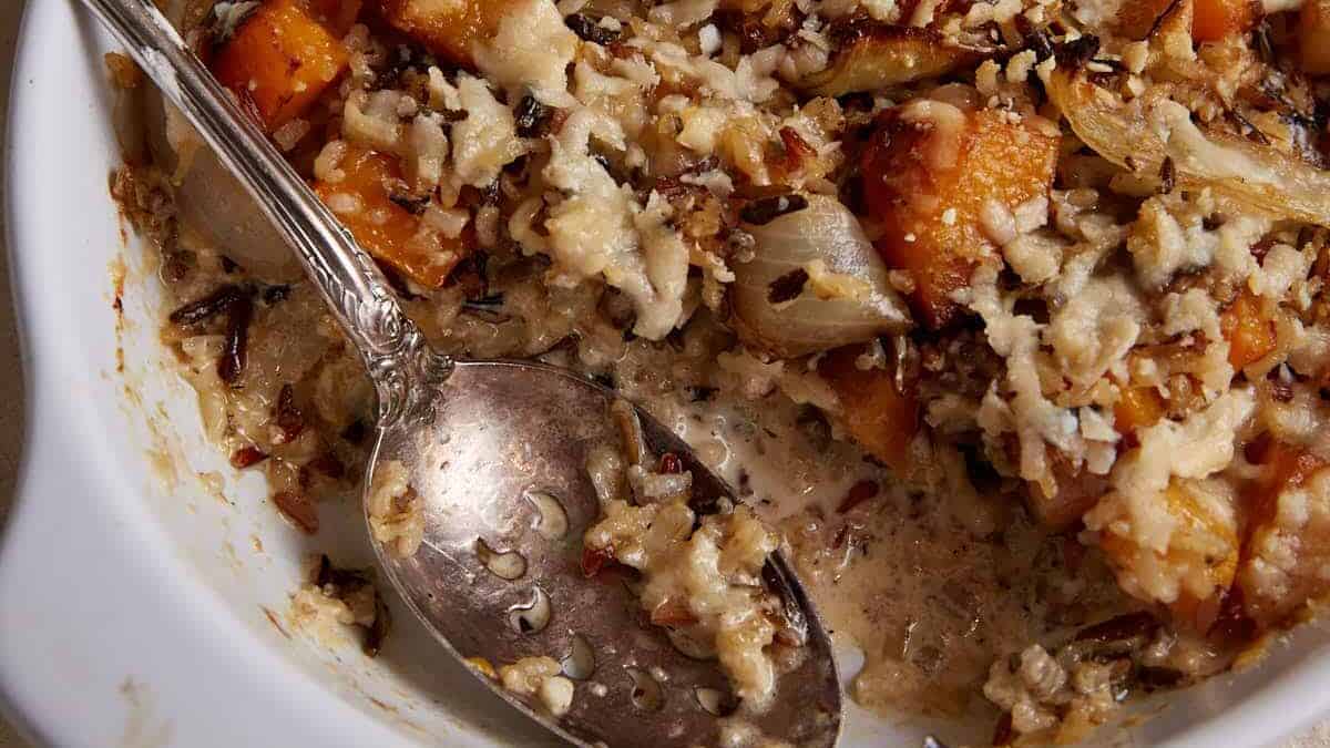 A serving spoon in a baking dish of butternut squash casserole.