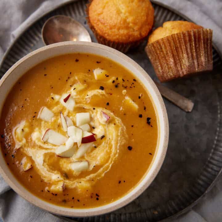 A bowl of butternut squash and apple soup with a swirl of sour cream.