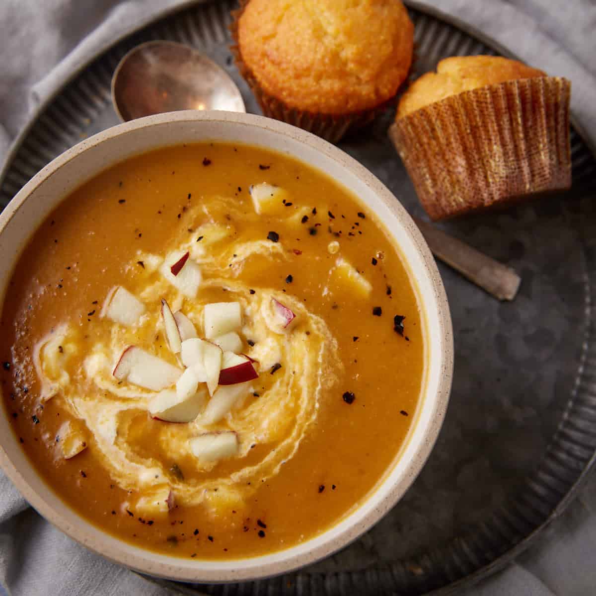 A bowl of butternut squash and apple soup with a swirl of sour cream.