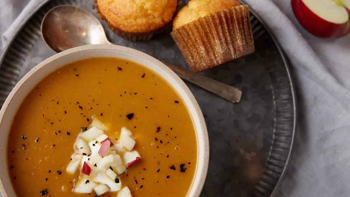 A bowl of butternut squash apple soup with apple chunks on top.