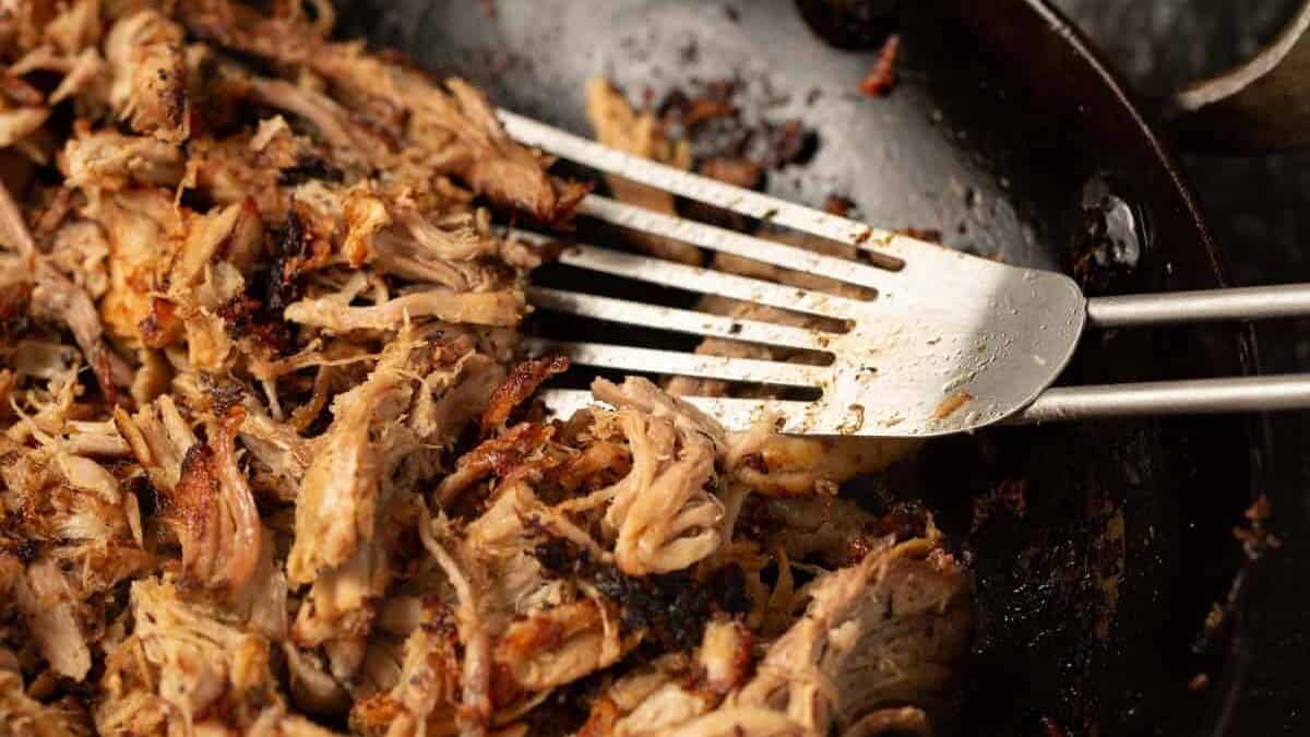 Crispy pork carnitas in a skillet with a spatula.