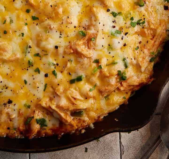 An iron skillet of chicken tamale pie next to serving spoons.