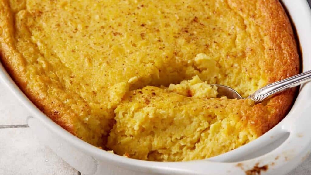 A baked corn pudding with a serving spoon removing a portion.