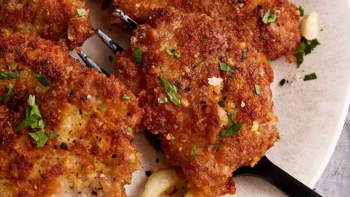 A serving fork removing a pork cutlet from a platter.