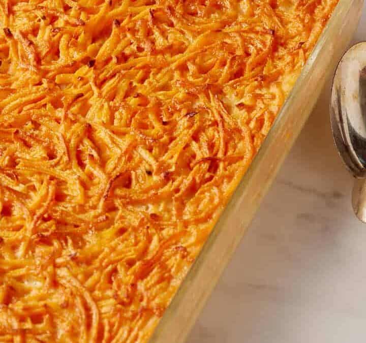 Sweet potato pudding in a casserole dish next to serving spoons.