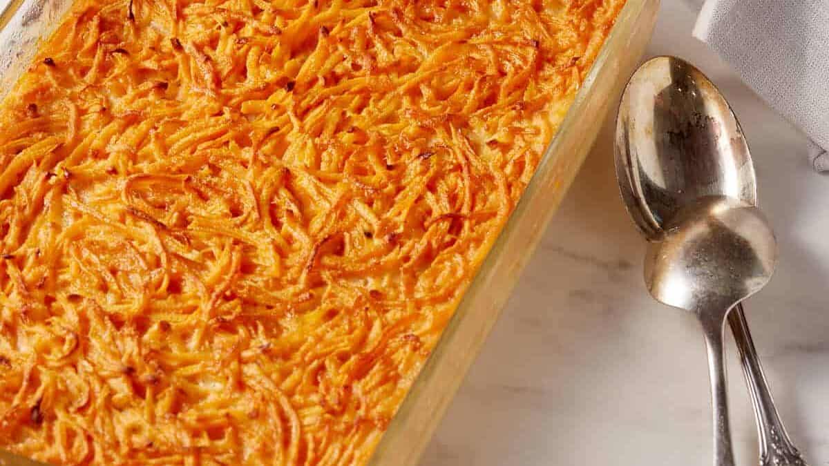 Sweet potato pudding in a casserole dish next to serving spoons.
