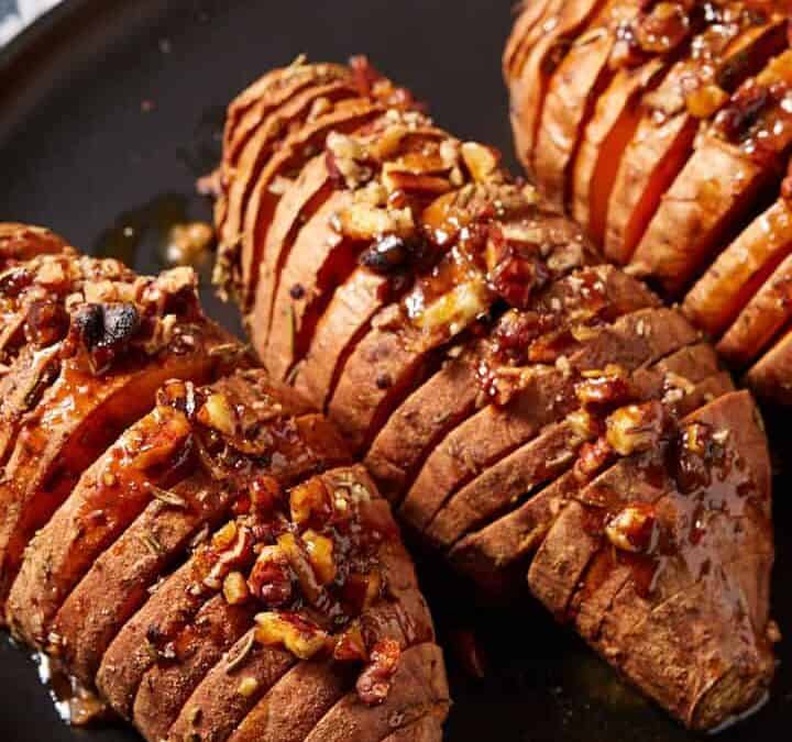 Hasselback sweet potatoes on a black platter with honey on the side.
