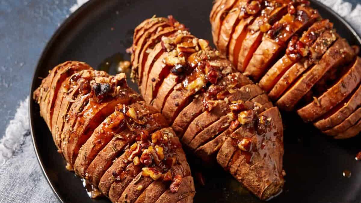 Hasselback sweet potatoes on a black platter with honey on the side.