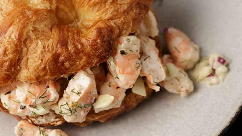 Shrimp salad on a croissant with dill on the side.