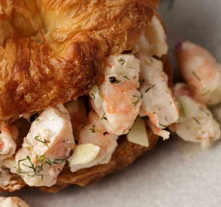 Shrimp salad on a croissant with dill on the side.