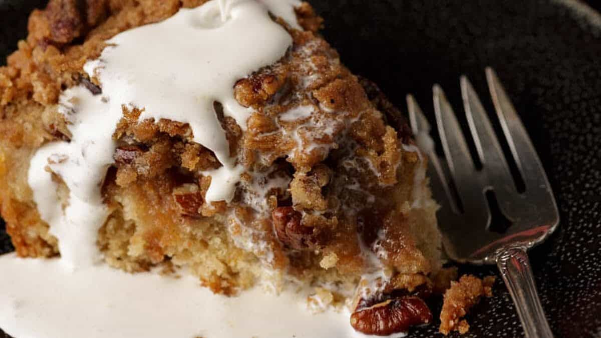 A slice of peach cake with cream being poured over the top.