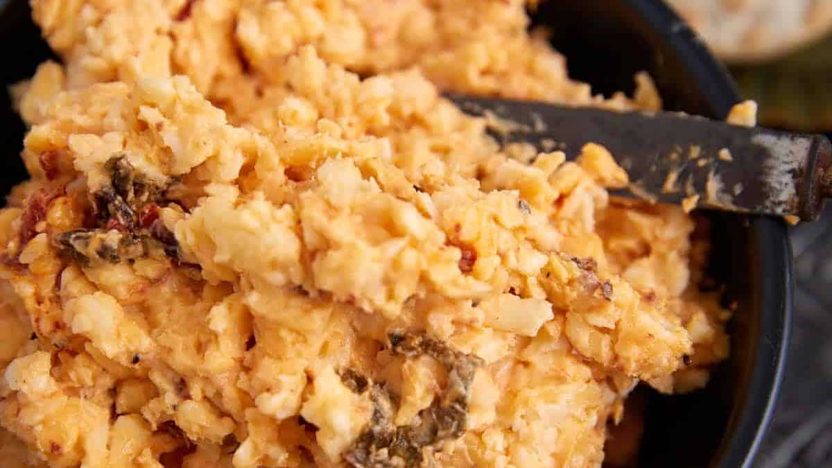 A bowl of pimento cheese with a spreading knife.