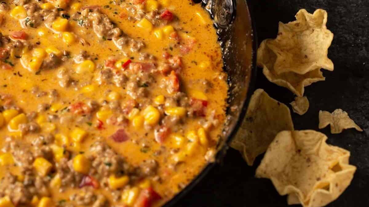 A skillet of pimento cheese dip next to a bowl of corn chips.
