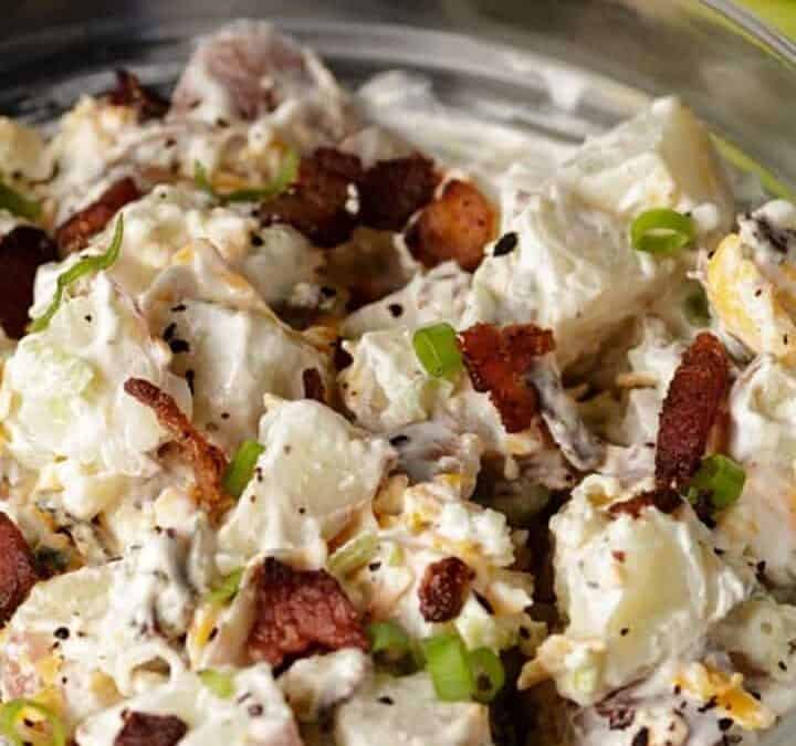 Southern style Ranch potato salad in a glass bowl next to green onions.