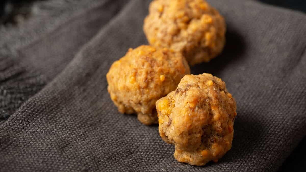 Three sausage balls on a grey napkin with a coffee cup next to it.