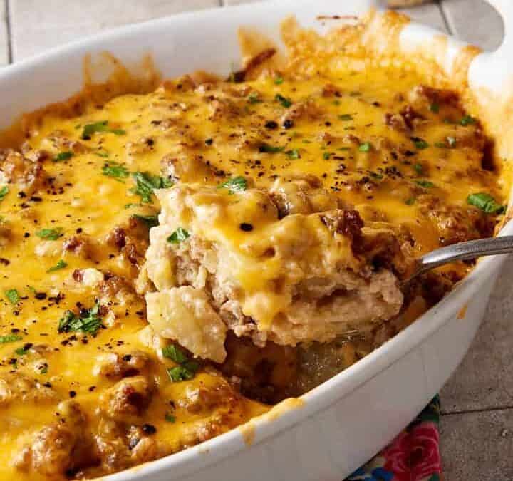 A sausage and potato breakfast casserole next to a coffee cup.