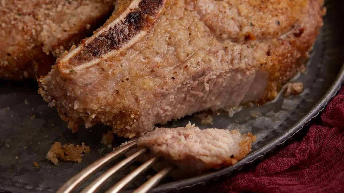 A fork with a bite of shake and bake pork chop.