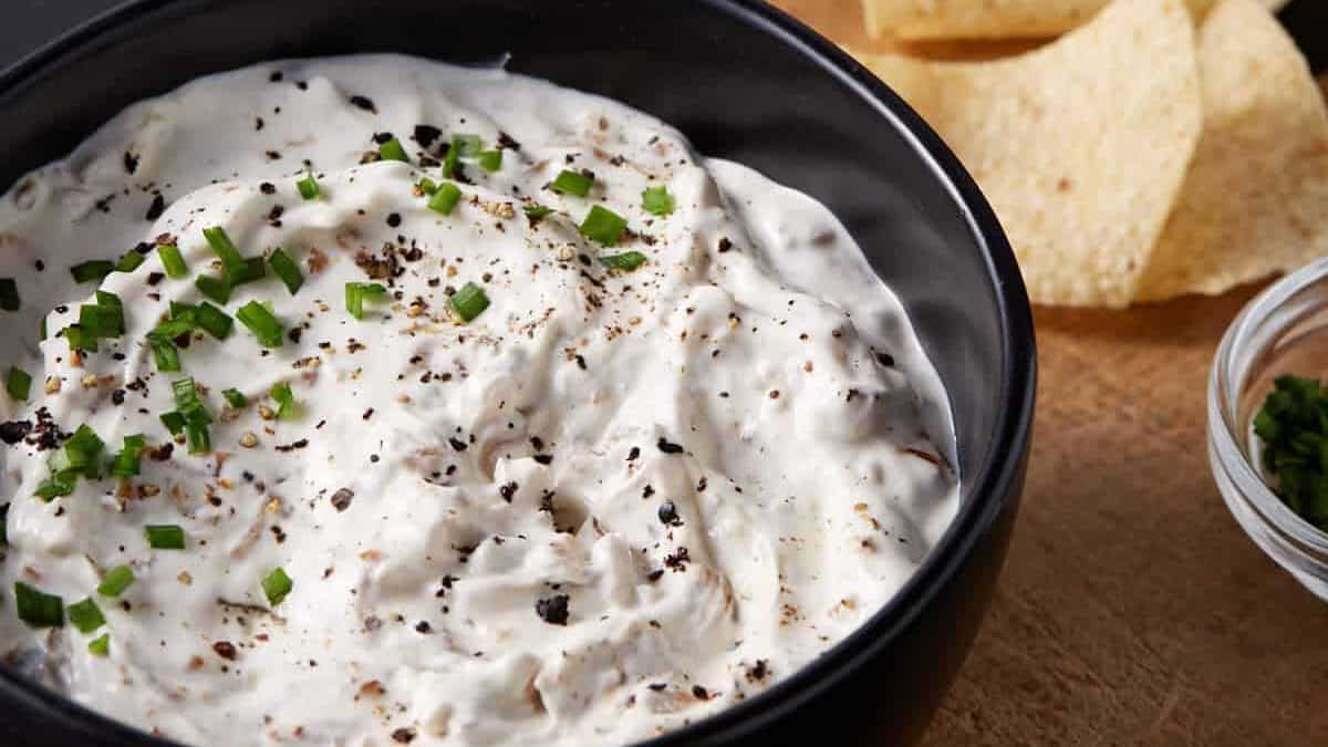 A bowl of sour cream dip with caramelized onions next to a bowl of chips.