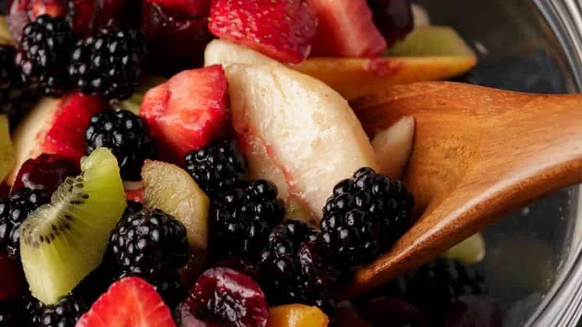 A bowl of spicy fruit salad with wooden spoon.