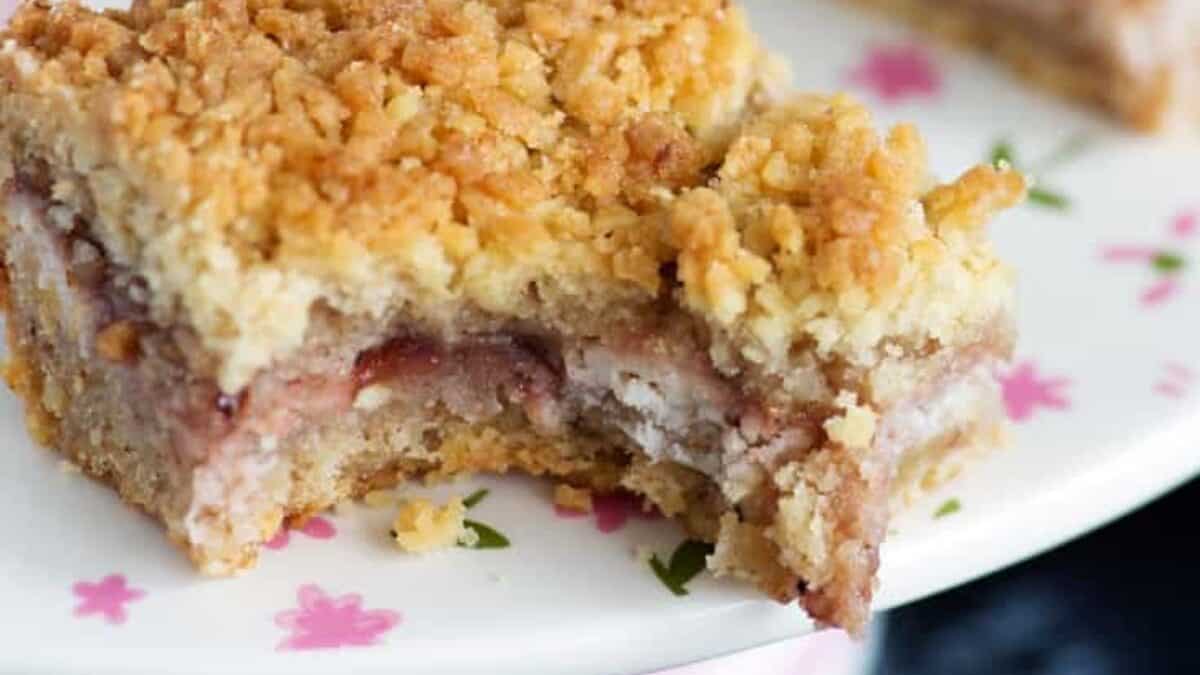 A close-up of a crumbly Dessert Bar with a fruity filling, missing a bite, resting on a white plate decorated with pink flowers.