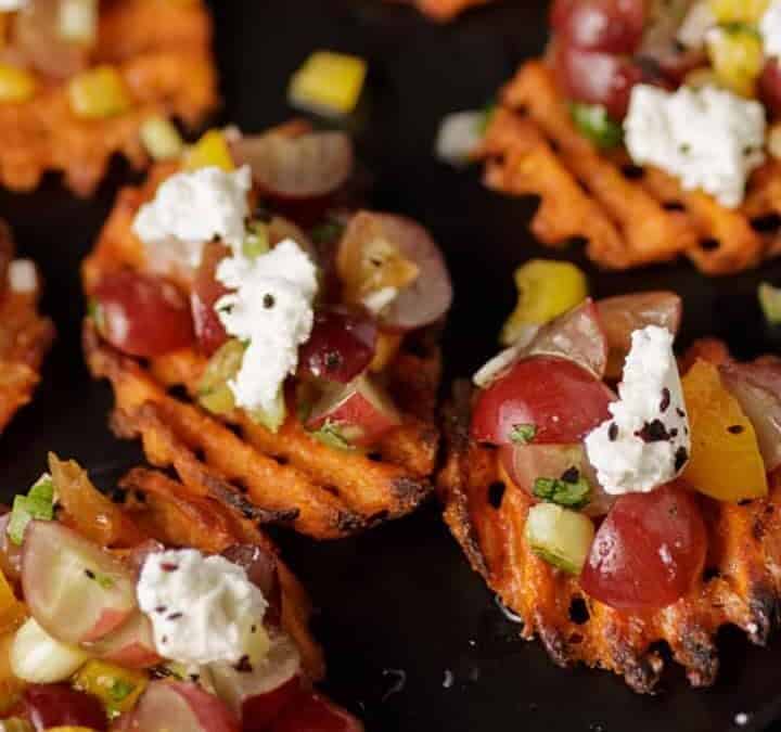 A platter of sweet potato appetizers next to glasses of wine.