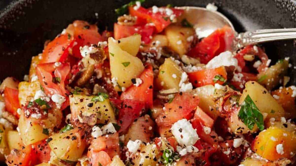 A black bowl of tomato salad with peaches and feta.