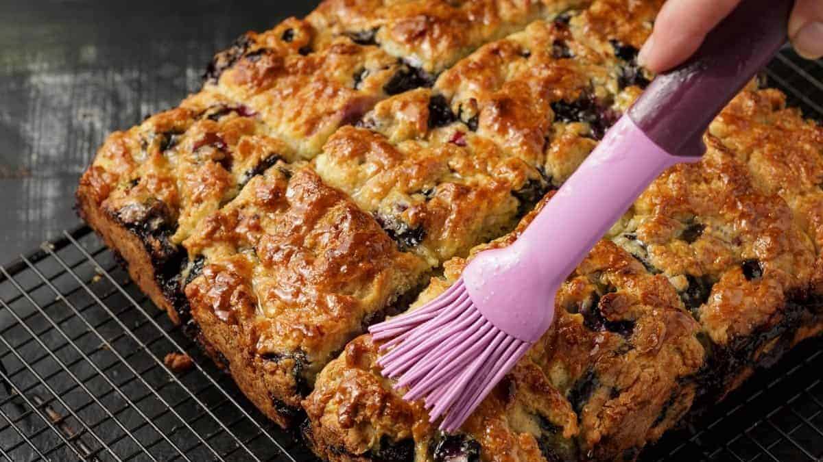 Honey glaze being brushed over blueberry biscuits.