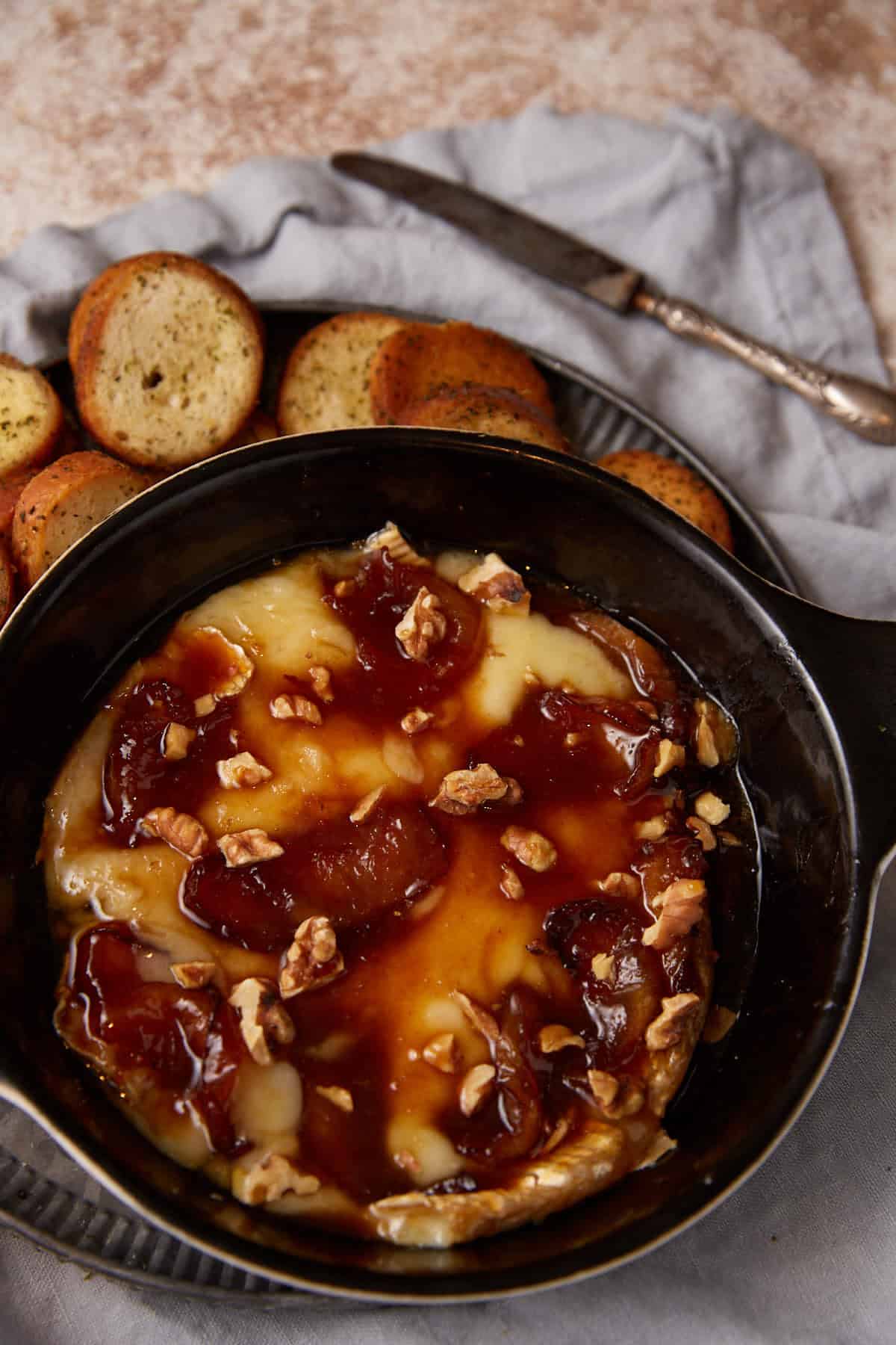 A dish of baked brie with apples next to crostini.