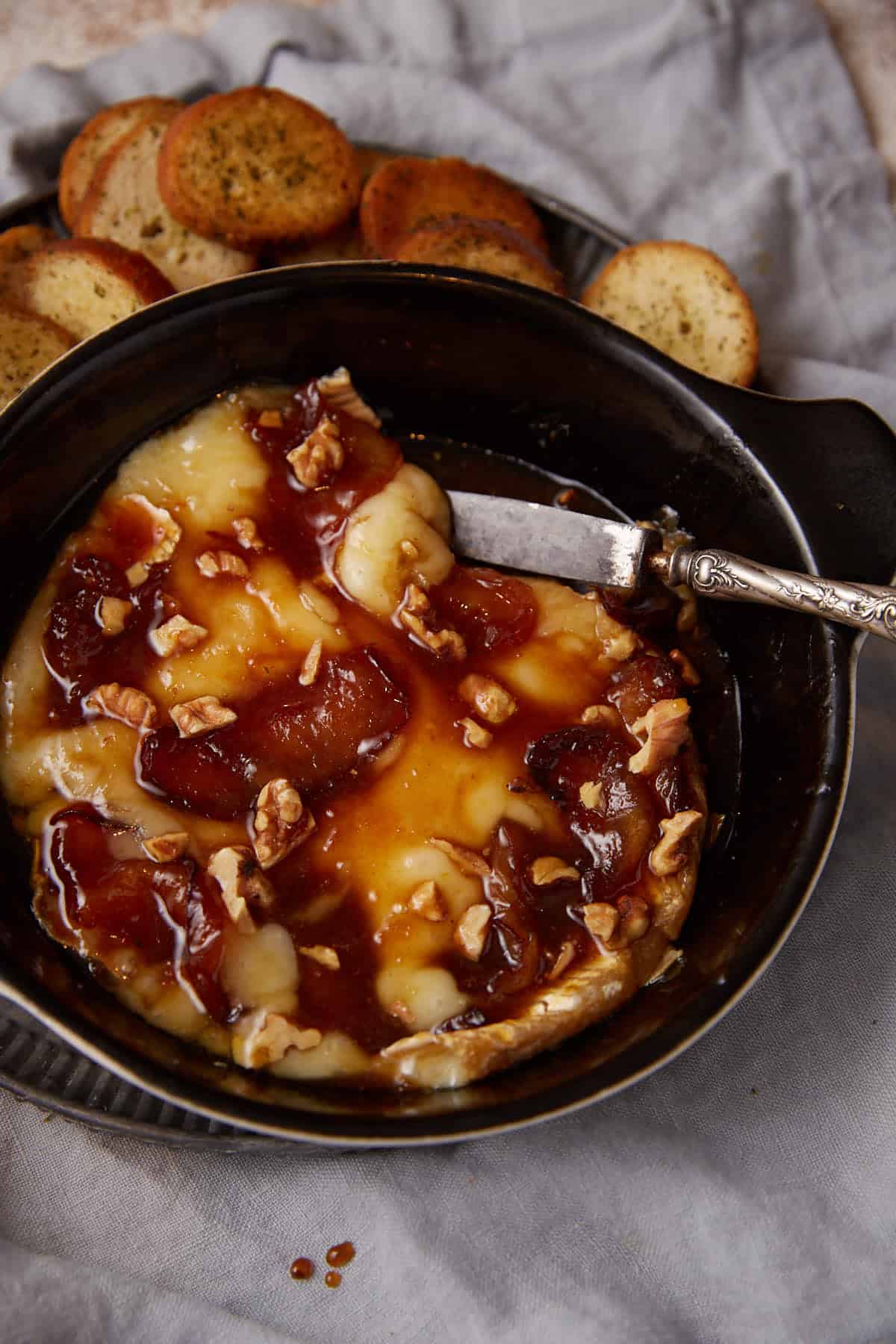 Baked brie with apples in a serving dish with a knife.