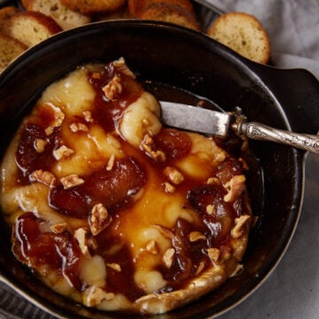 A serving dish with baked brie covered in apples and walnuts.