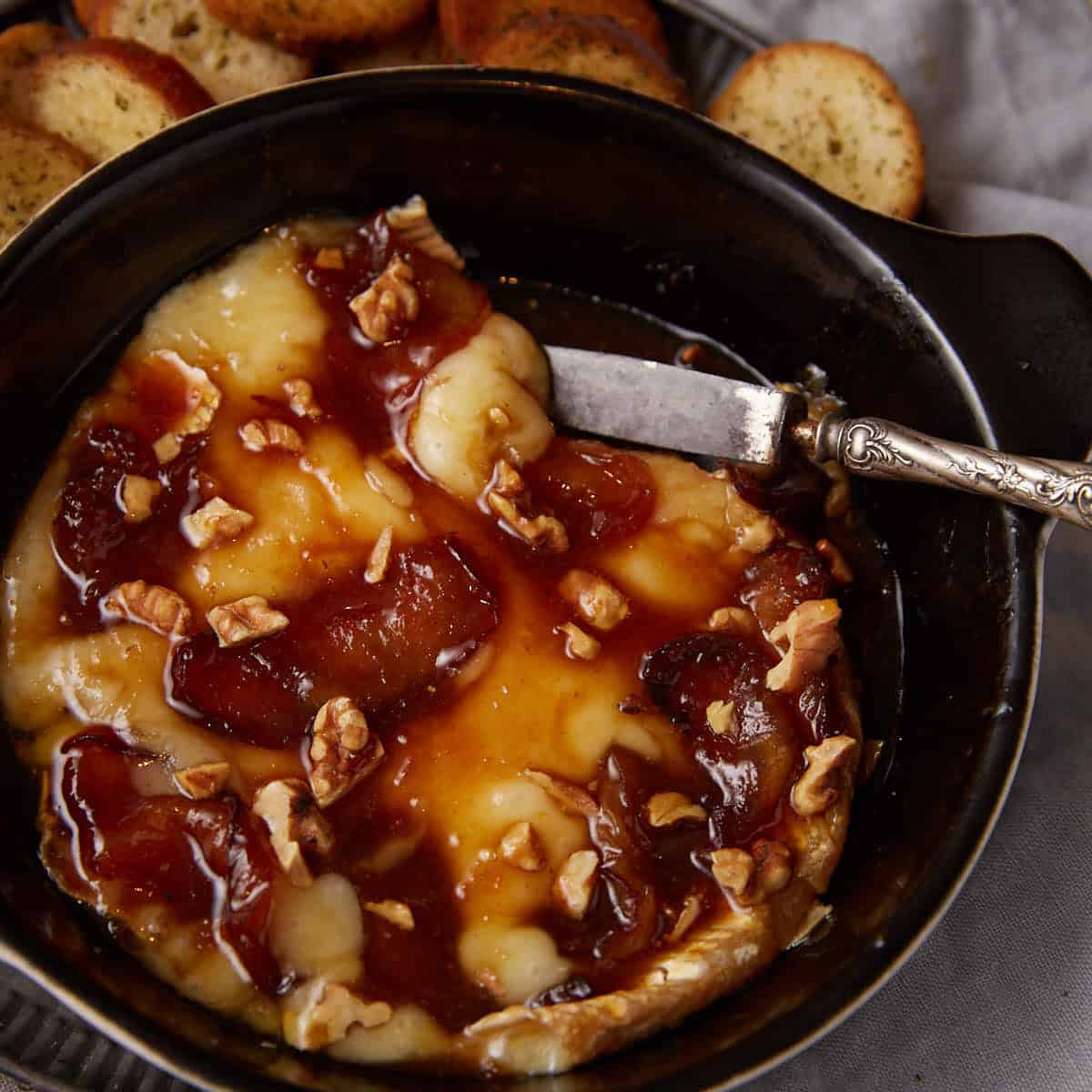 A serving dish with baked brie covered in apples and walnuts.