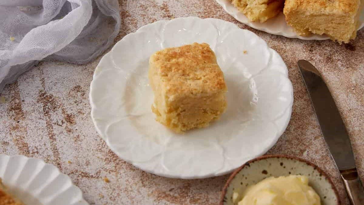 A single butter biscuit next to a platter of biscuits.