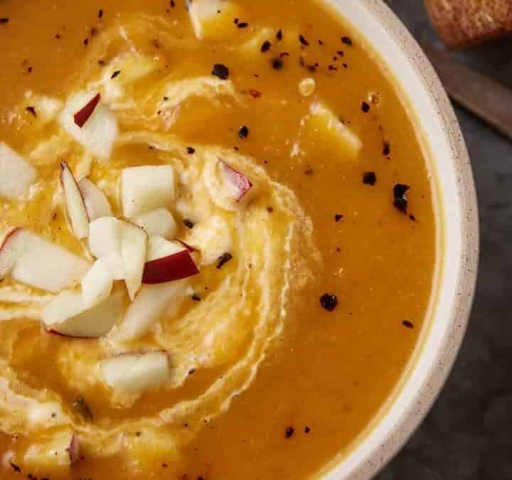 A bowl of butternut squash and apple soup with a swirl of sour cream.