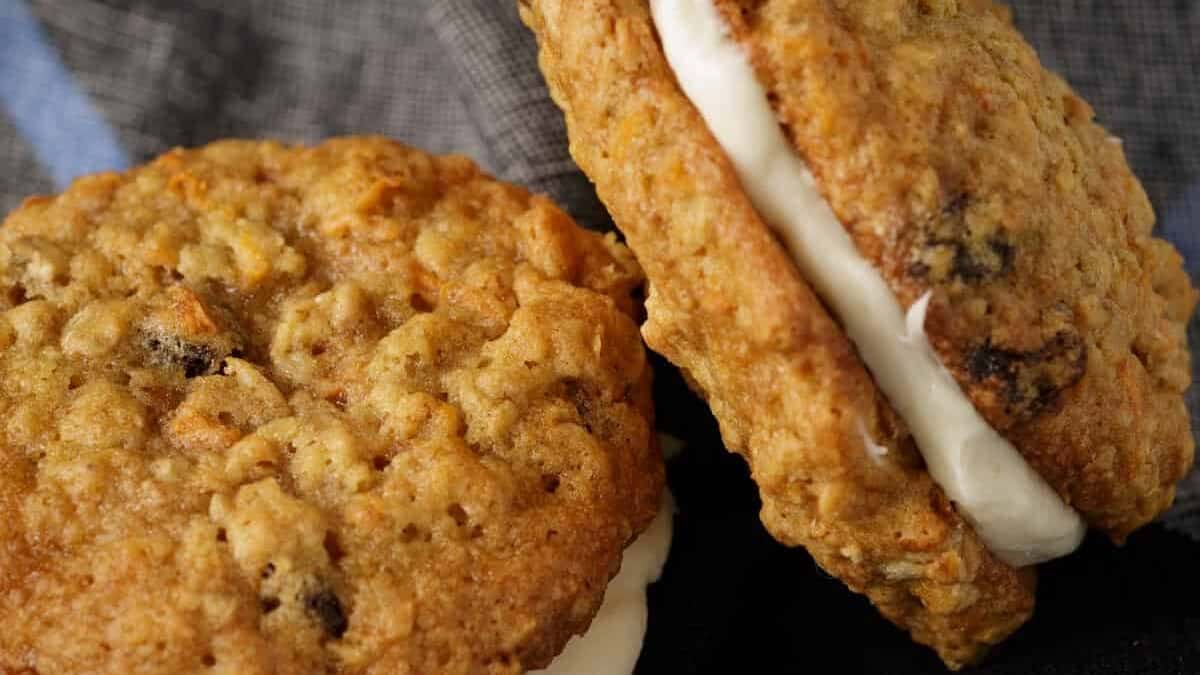 Two carrot cake sandwich cookies propped up and laying on a napkin