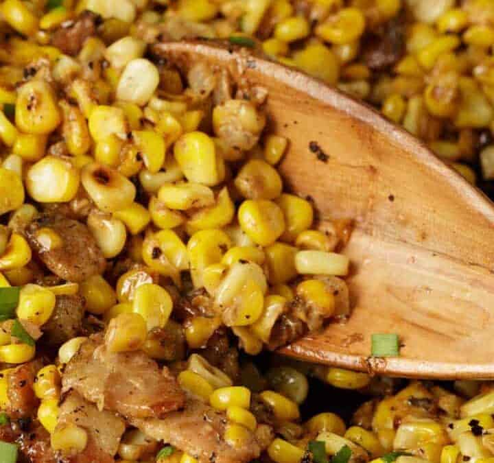 Cooked corn in a skillet with a wooden spoon.