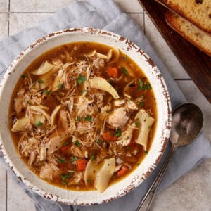 A bowl of chicken soup next to toasted bread.