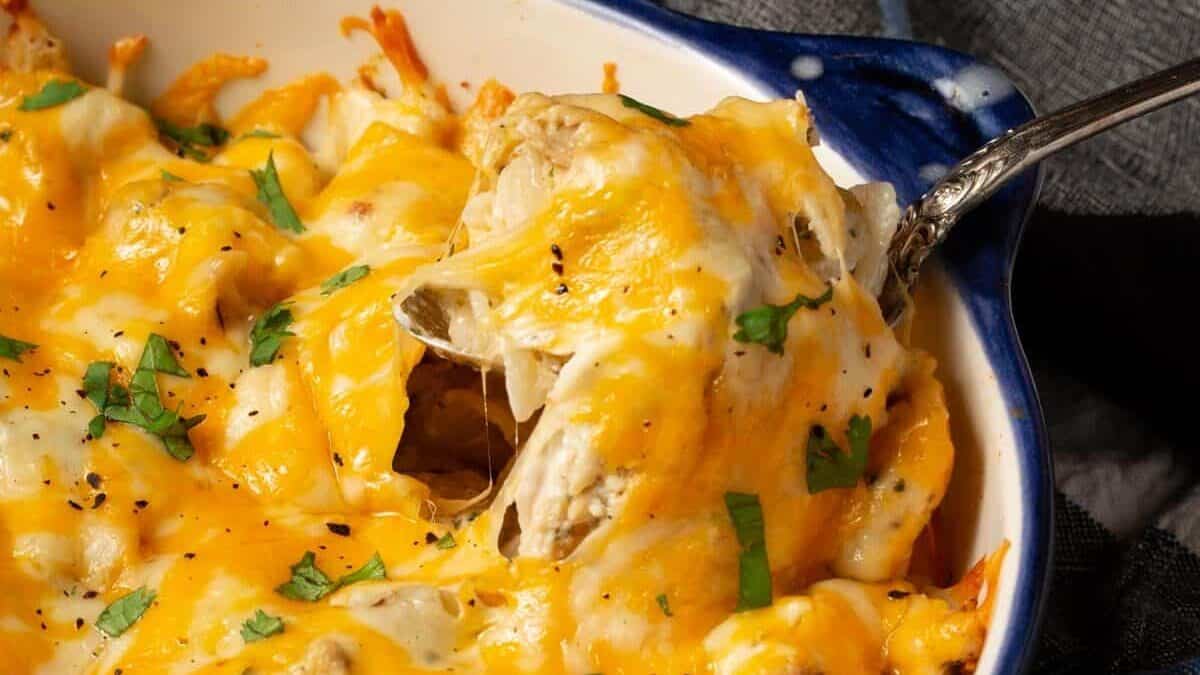 A spoon in a dish of baked pasta with cheese on top.