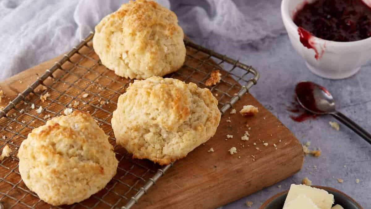 Three drop biscuits next to some jam, honey and butter.