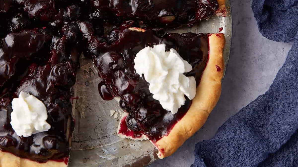 A pie pan of fresh blueberry pie topped with whipped cream.