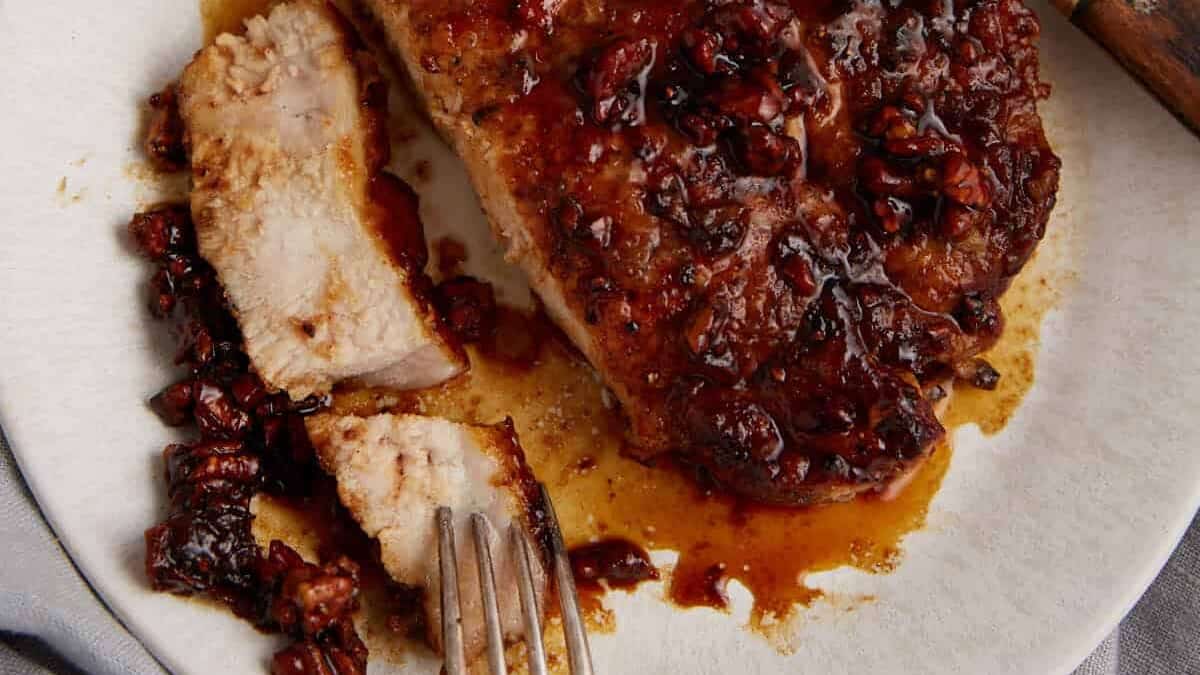 A honey glazed pork chop on a plate with a knife and fork.