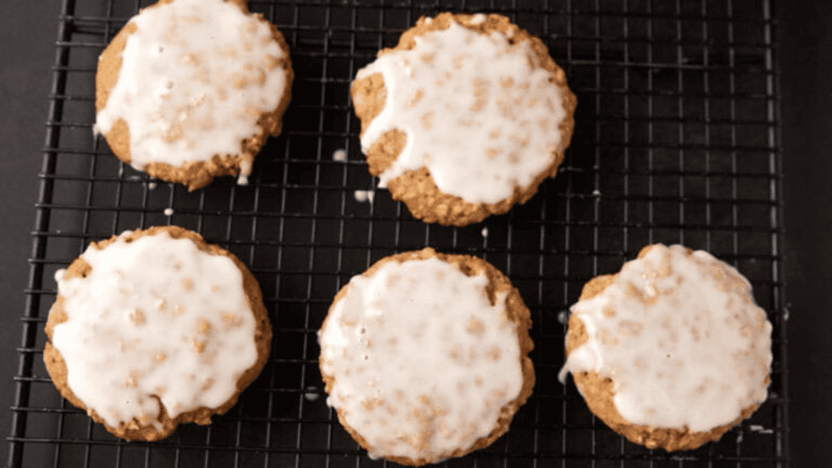 Five round cookies with white icing are arranged on a black wire cooling rack, viewed from above. Perfect as potluck desserts, the icing covers most of each cookie, and the background is dark.