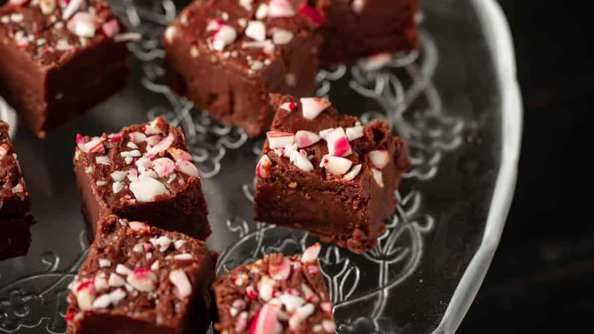 Fudge with candy canes on a platter with greenery in the background.