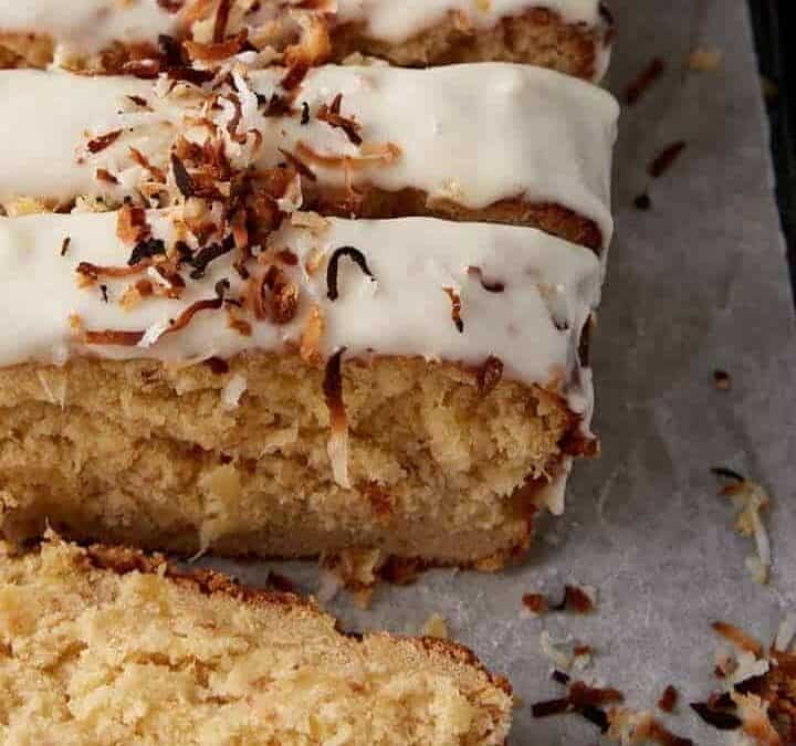 A loaf of coconut bread with frosting and coconut flakes.