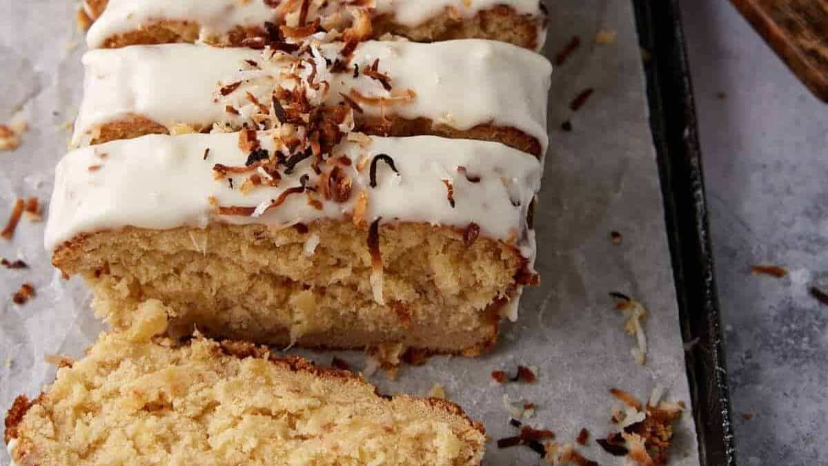 A loaf of coconut bread with frosting and coconut flakes.